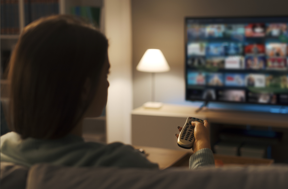 A woman sitting in front of a TV, holding a remote and looking through shows on Netflix